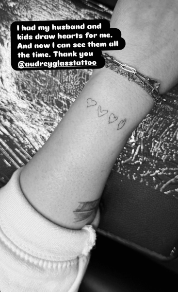 Black and white image of Jennifer Love Hewitt's forearm featuring a tattoo of four hearts and a cluster of bracelets